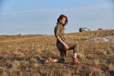 Arka planda araba, seyahat ve doğa konsepti, uzak yerlerin güzelliği ile tarlanın ortasında oturan bir kadın.