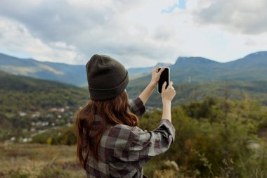 Manzaralı bir seyahat macerası sırasında akıllı telefonuyla görkemli dağ sırasının nefes kesici görüntüsünü yakalayan bir kadın.
