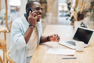 Erkek masa başı iş adamı telefon bilgisayarı işinde çalışıyor. Genç teknoloji dizüstü bilgisayarcı. Çalışan yetişkin masa başı iletişimi konuşuyor.