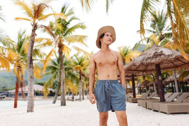 Tropikal plajda gülümseyen Asyalı adam, Deniz Tatilinin tadını çıkarıyor.