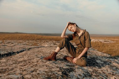 Sahada kayanın tepesinde oturan sakin bir kadın. Yolculuk macerası fotoğrafında elleri başının üstünde.