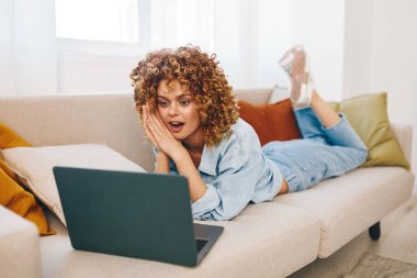 Ev bilgisayarında çalışan gülümseyen kadın rahat oturma odasında serbest yaşam tarzının tadını çıkarıyor.