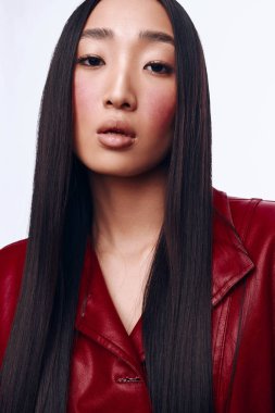 Kırmızı deri ceketli, uzun siyah saçlı güzel Asyalı kadın beyaz arka planda kameraya poz veriyor.