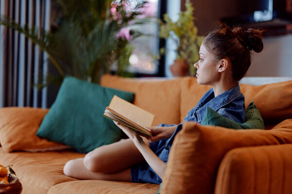 Woman Sitting on Couch Reading Book in Living Room with Coffee Table in Front of Her