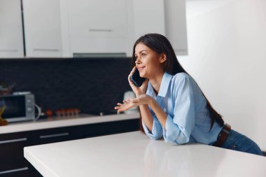 Modern evdeki mutfak tezgahında telefonla konuşan kadın. Parlak ve çağdaş iç tasarım konsepti.