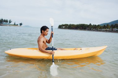 Mutlu Asyalı Adam Tropikal bir plajda kanoyla eğleniyor.