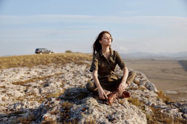 Yolculuk macerasında kayanın üzerinde oturan bir kadın güzel manzaralı ve gökyüzüyle