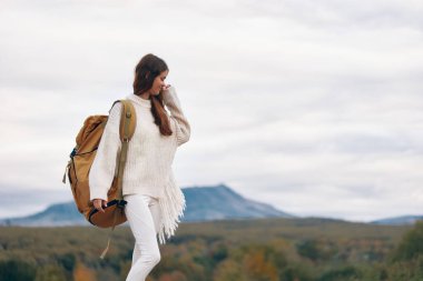 Sırt çantasıyla maceralı bir dağ yürüyüşünde gülümseyen kadın, manzaranın ortasında doğa ve özgürlüğün tadını çıkarıyor.
