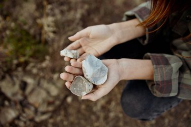 Ellerinde taşlarla yerde oturan iki kişi, doğa keşfi ve farkındalık kavramı.