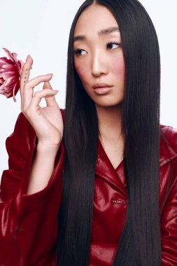 Siyah saçlı, kırmızı deri ceketli, elinde çiçekle gezen çekici bir genç kadın.