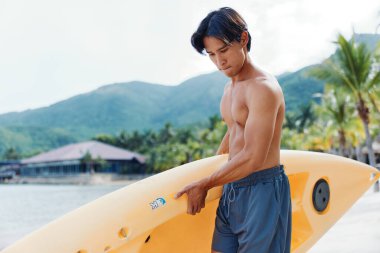 Tropik cennette kano süren bir adam, Palmiye püsküllü bir plajda yaz tatilinin tadını çıkarıyor..