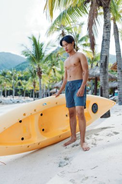 Mutlu Asyalı adam kayak yapıyor ve tropik sahilde yaz tatilinin tadını çıkarıyor.