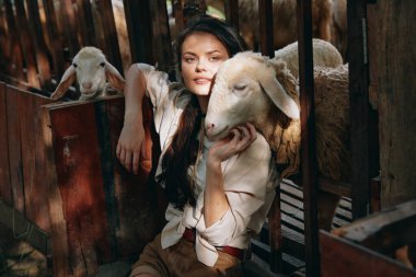 Arka planda koyun olan bir kadın çitin önünde oturuyor.