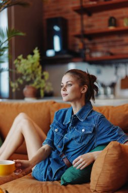 Arka planda bir bitki ve bir fincan kahveyle koltukta dinlenen bir kadın.