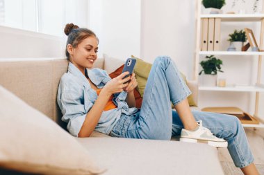 Kanepe Sakinleri Zevki: Cep telefonunu tutan mutlu bir kadın, Evinin Konforu 'ndaki koltukta dinleniyor, Çevrimiçi Oyunlara katılıyor ve Selfie çekiyor