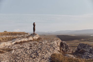 Dağın tepesinde uzanmış kollarıyla duran bir adam, aşağıdaki vadiyi düşünüyor görkemli yolculuk anında.