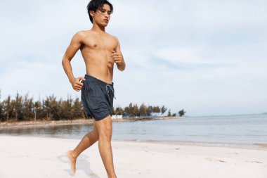 Kaslı Asyalı sporcu Sunset plajında kardiyo çalışmasının keyfini çıkarıyor.