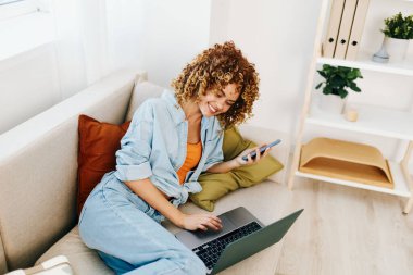 Modern bir oturma odasında dizüstü bilgisayarda çalışan gülümseyen bir kadın.