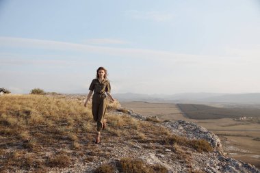 Yeşil elbiseli bir kadın tarlada duruyor, doğanın güzelliği ve moda uyumu.