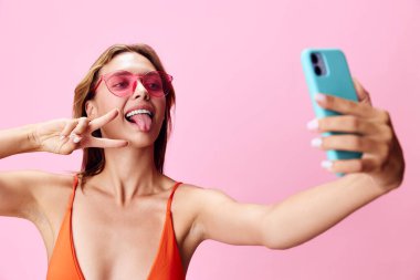 Güneşli ve mayolu bir kadın pembe duvarın önünde selfie çekerken aptal bir poz veriyor.