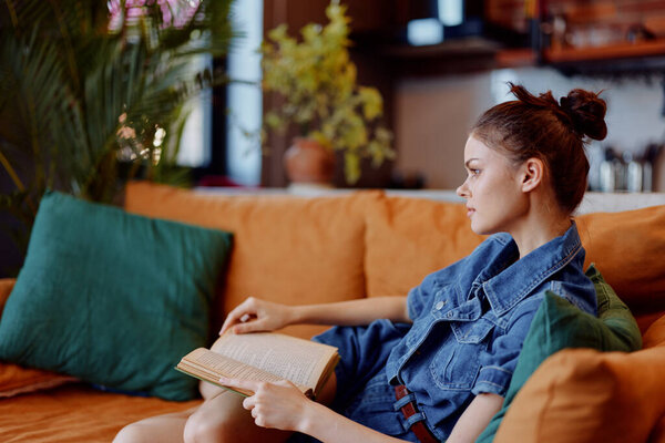 Woman sitting on orange couch with crossed legs reading book in cozy home interior concept
