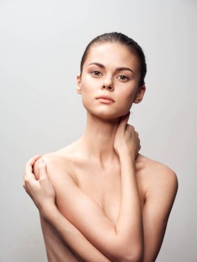 Çıplak poz veren, elleri omuzlarında, gülümseyen kameraya bakan şehvetli ve kendinden emin genç bir kadın.