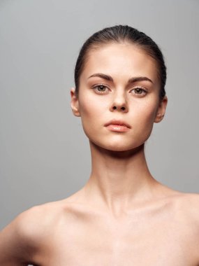 Temiz tenli, makyajsız, stüdyo ortamındaki gri arka planda izole edilmiş genç bir kadının doğal güzel portresi.