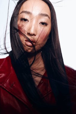 Uzun siyah saçlı, kırmızı ceketli, profesyonel bir fotoğraf çekimi için poz veren güzel bir genç kadın.