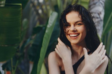 Güneşli bir günde yemyeşil bitkilerin ve tropikal bahçede palmiye ağaçlarının yanında duran mutlu kadın.