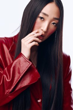 Uzun siyah saçlı, kırmızı deri ceketli, kendine güvenen Asyalı kadın. Yüz yüze poz veriyor.