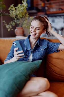 Mutlu kadın kanepede oturup telefonla gülümsüyor.