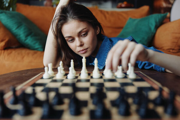 Young woman playing chess on wooden table in front of brown couch in cozy living room