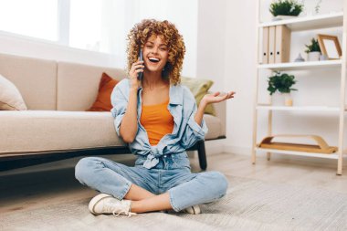 Neşeli kadın cep telefonunu tutuyor, rahat oturma odasında koltukta dinleniyor.