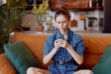 Kot gömlekli genç kadın rahat atmosferde telefonuna bakıyor.