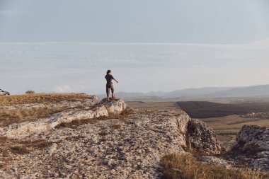 Dağın tepesinde duran ve kollarını açıp vadiye bakan bir adam görkemli seyahat sahnesinde.