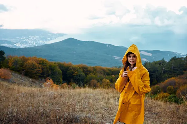 stock image A woman in a stylish yellow raincoat enjoying the stunning view of the mountains on a peaceful hilltop retreat