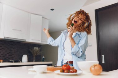 Mutfakta şarkı söyleyen mutlu kadın bıçakla taze domates hazırlıyor.