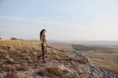 Tepede çantalı ve şapkalı bir kadın, zarif ve güzel bir dokunuşla geziyor.