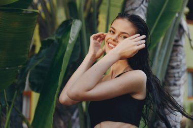 Palmiye ağacının önünde dalgalı saçları olan genç bir kadın tropikal tatilde siyah sutyen giyiyor.