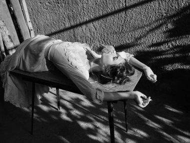 Ağzında sigarayla baştan çıkarıcı bir kadın siyah beyaz bir şekilde masaya yaslanıyor.