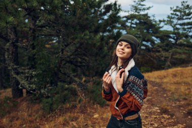 Şık şapkalı ve kazaklı bir kadın huzurlu ormanda sonbaharın canlı renklerini keşfediyor.