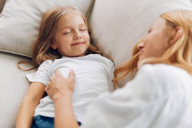 Anne ve kızı sıcak, davetkar bir oturma odasında sıcak bir kanepede sevgi dolu bir kucaklaşmayı paylaşıyorlar.