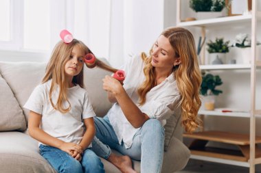 Anne ve kızı rahat bir kanepede pembe saç bigudileriyle gülüşüp gülüyorlar.