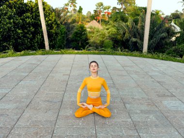 Turuncu elbiseli kadın, kalabalık şehir manzarasıyla çevrili avluda yoga yapıyor, kaos içinde huzur buluyor..