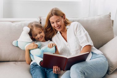 Anne ve kızı rahat oturma odasındaki kanepede kitap okuyarak güzel vakit geçiriyorlar.