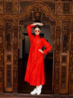 Çarpıcı kırmızı elbiseli sofistike bir kadın güzel detaylı ahşap bir kapının önünde duruyor..