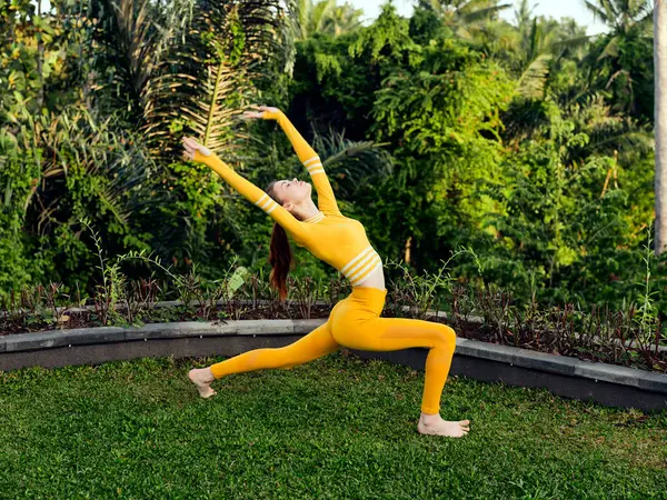 stock image A woman in a vibrant yellow outfit peacefully practices yoga on lush green grass, embodying tranquility and balance.