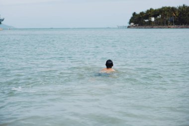Yüzmek, Rahatlamak ve Yenilenmek: Mavi Okyanus 'un Tropikal Sahil Tatilinde Eğlenen Neşeli Bir Asyalı Adam