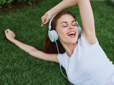 Yazın yeşil çimenlerin üzerinde kulaklıklarla uzanan kadın mutluluğu gülümsemesi. Yüksek kalite fotoğraf