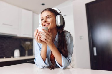 Mutfakta kahve ve müzik dinleyen, kulaklıklı bir masada oturan genç bir kadın.